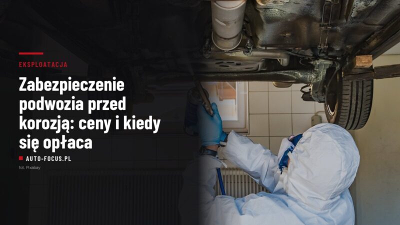 Mechanik w kombinezonie natryskuje preparat antykorozyjny na podwozie samochodu na podnośniku